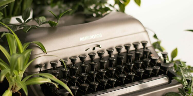 Eine grüne Pflanze in einem weißen Blumentopf steht neben einer Schreibmaschine